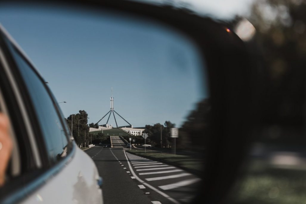 Parliament House viewed within a side view mirror of a car